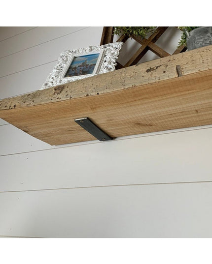 Black steel L-shaped shelf bracket supporting rustic reclaimed wood floating shelf with decorative items on white shiplap ...