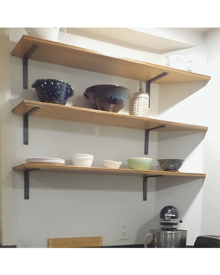 Black steel L-shaped shelf brackets supporting natural wood floating shelves in modern kitchen with dishes and bowls displ...