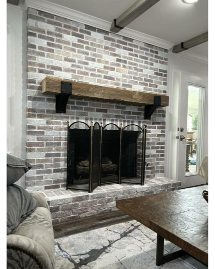 Black metal Mottville mantel brackets supporting rustic wood beam above brick fireplace in modern farmhouse living room by...