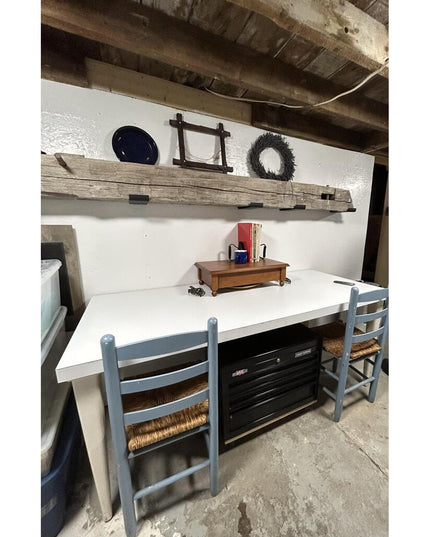 Rustic weathered wood beam mounted as floating shelf above white desk workspace with blue chairs, featuring dark metal Gli...