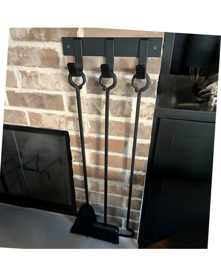 Black metal Mary Style Handmade Coat Rack by Industrial Farm Co with three wall-mounted hooks holding fireplace tools agai...