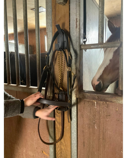 Black metal Elizabeth Wall Hook by Industrial Farm Co holding horse bridle in stable, hands adjusting leather straps, rust...