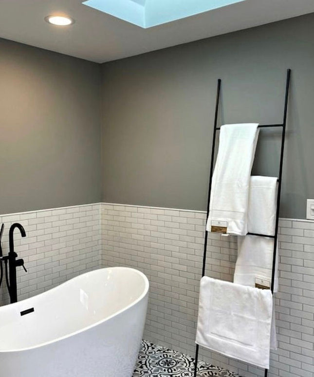 Black metal ladder towel rack by Industrial Farm Co displayed in modern bathroom with white subway tile and freestanding tub