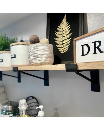 Black metal Nauseef shelf support brackets holding natural wood floating shelf with decorative items and fern artwork