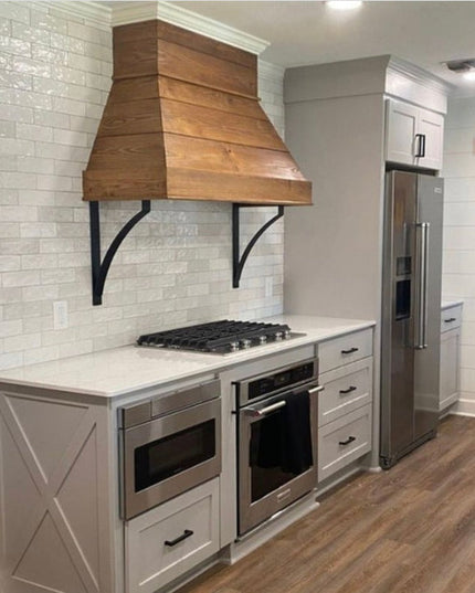 Syracuse black metal countertop support brackets holding wooden range hood in modern farmhouse kitchen with white subway t...