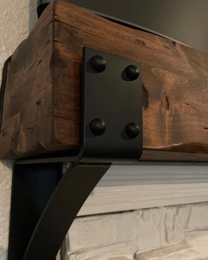 Heavy duty black steel Spafford mantel bracket with decorative rivets supporting reclaimed wood beam above white brick fir...