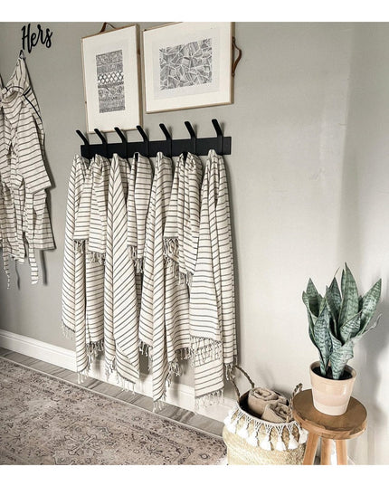 Black wall-mounted Fairmount Style Coat Rack by Industrial Farm Co with 7 hooks holding white striped towels, displayed in...