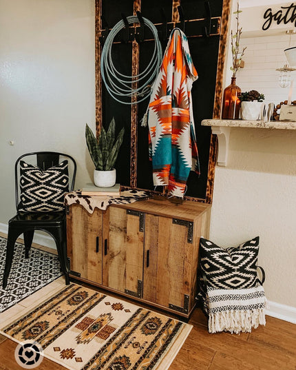 Rustic wooden cabinet with ornate mirror displaying colorful Southwestern blanket, rope, and tribal patterned pillows in b...