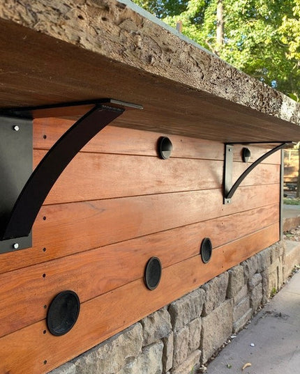 Heavy duty black steel Albany shelf brackets supporting reclaimed wood shelving on stone wall with circular entry holes fo...