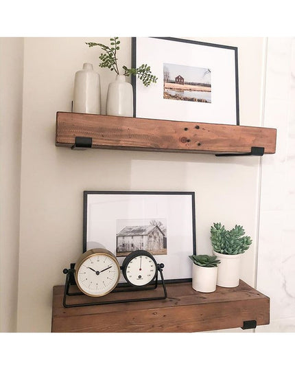 Rustic wood floating shelves with black metal brackets displaying white ceramic vases, succulents, framed barn artwork, an...
