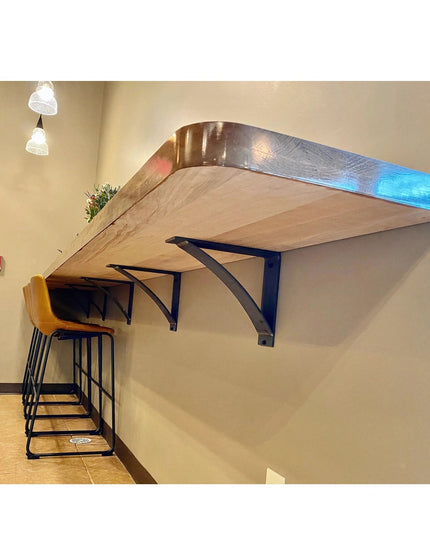 Black Hattie Style curved metal bracket supports holding floating wood shelf with yellow bar stools underneath by Industri...