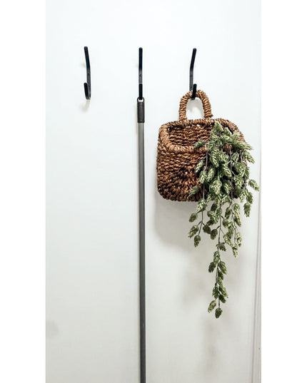 Black metal Stewart 1/2" Wide Double Hook by Industrial Farm Co mounted on white wall holding woven basket with trailing g...