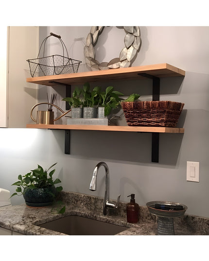 Black steel L-bracket shelf supports holding natural wood floating shelves above kitchen sink with plants and decorative i...
