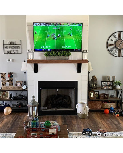 Rustic wooden mantel with black metal brackets supporting TV above white brick fireplace in modern farmhouse living room