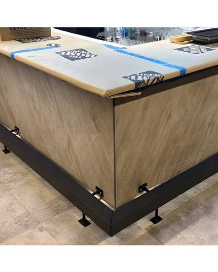 Black metal bar foot rail brackets mounted on wood-grain kitchen island base with white countertop during installation