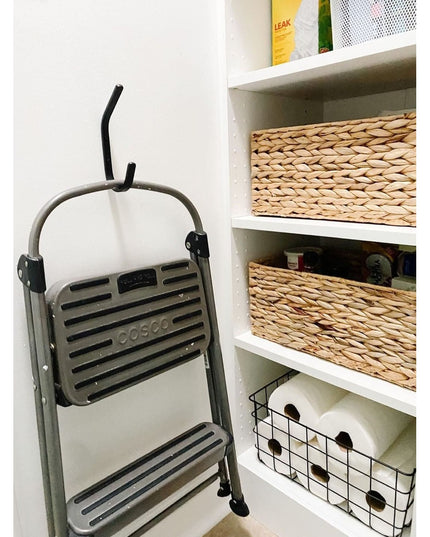 Black metal double hook mounted on white pantry wall holding folded gray Cosco step stool, with wicker storage baskets on ...