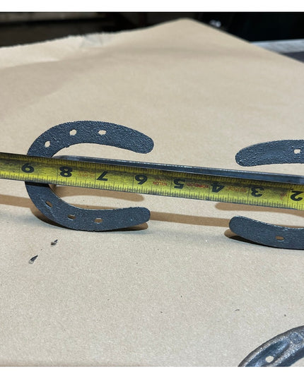 Black horseshoe door handles being measured with tape measure on wooden surface - Chincoteague Pony Shoe style by Industri...