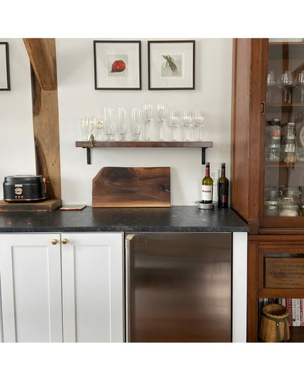 Black steel L-shaped shelf brackets supporting dark wood floating shelf with glassware in modern farmhouse kitchen with ex...