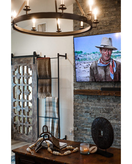 Black metal Wall Mounted Ossit Ladder by Industrial Farm Co displaying folded blankets in rustic living room with stone fi...