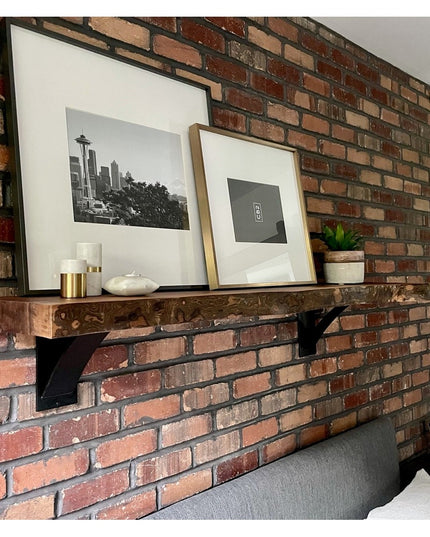 Industrial black steel shelf brackets supporting wooden floating shelf on exposed brick wall with framed artwork and decor...
