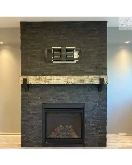 Rustic wooden beam mantel with black steel Spafford brackets mounted on dark stone fireplace surround by Industrial Farm Co