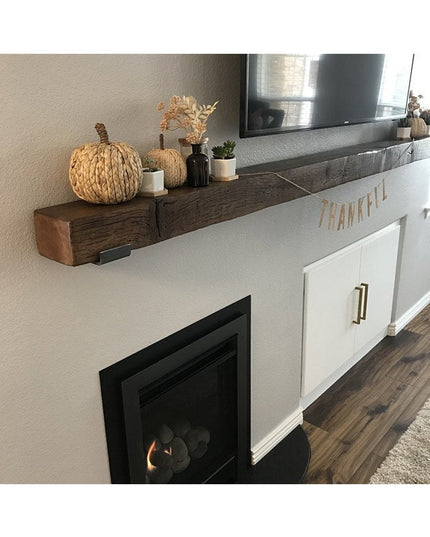 Dark wood floating shelf with black steel J brackets mounted above white fireplace mantel, decorated with woven pumpkins a...