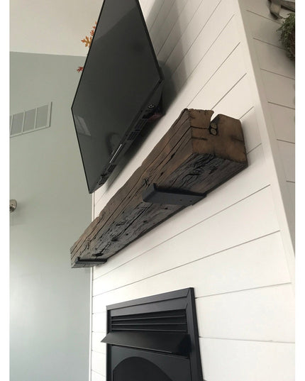 Rustic reclaimed wood beam floating shelf mounted on white shiplap wall with black TV above, supported by steel J brackets...