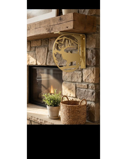 Handcrafted brass-colored metal elk profile L-bracket shelf support mounted on rustic stone fireplace with wooden beam man...