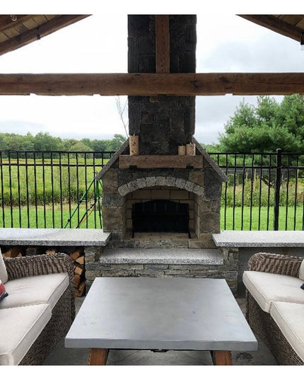 Rustic wooden fireplace mantel with exposed beam ceiling on covered outdoor patio featuring wicker seating and stone const...