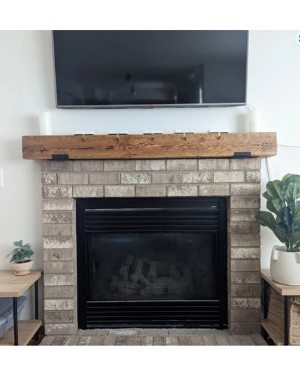 Rustic wooden mantel with black metal J-bracket supports mounted above brick fireplace with TV, showcasing The Glimmerglas...