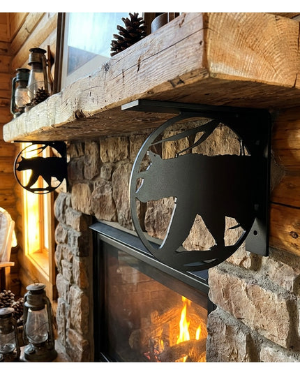 Black metal bear silhouette L-bracket shelf support holding rustic wood mantel above stone fireplace in log cabin interior