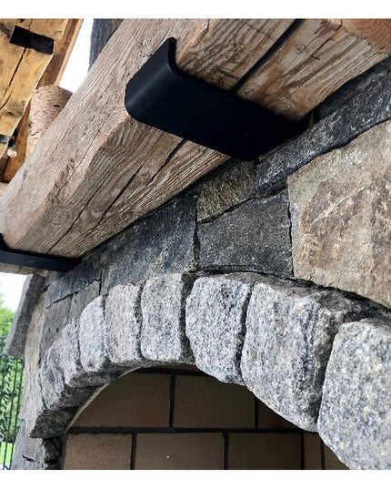 Black metal Glimmerglass J Shelf Bracket by Industrial Farm Co supporting rustic wood beam against stone archway wall