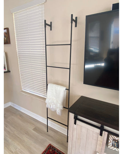 Black metal Brielle Top Mounted Blanket Ladder by Industrial Farm Co mounted on beige wall with white throw blanket in mod...