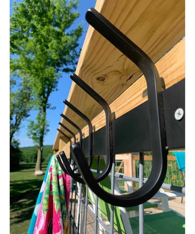 Black metal Eastman Coat & Hook Rack mounted under wooden pergola with colorful towel hanging, showing curved hook design