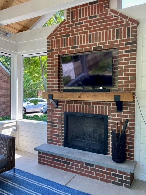 Red brick outdoor fireplace with reclaimed wood mantel held by black Kudlick farmhouse mantel brackets on a covered patio