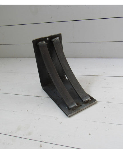 Black metal corbel bracket with curved design from Industrial Farm Co displayed on white wooden planks