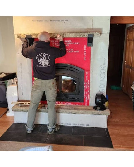Worker installing black iron Fulton Style Heavy Duty Mantel Support brackets on white stone fireplace mantel during constr...