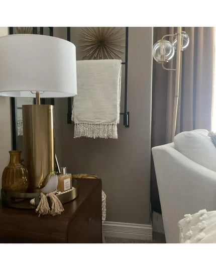 Modern bedroom interior featuring brass table lamp with white shade, decorative wall art, and white upholstered chair in n...