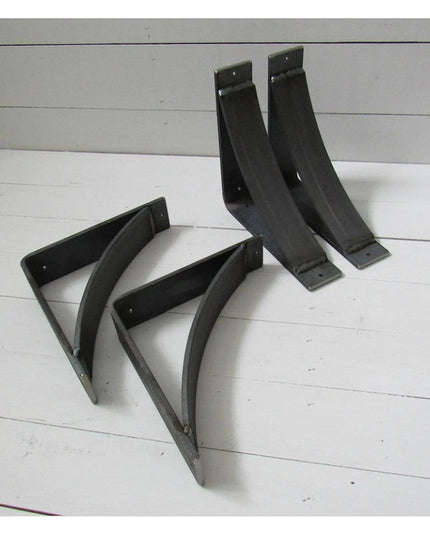 Black metal Hattie Style curved shelf bracket supports by Industrial Farm Co displayed on white wooden background, showing...