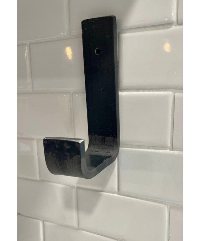 Black metal Western Ridge 1.5" J Wall Hook by Industrial Farm Co mounted on white subway tile backsplash showing curved ho...