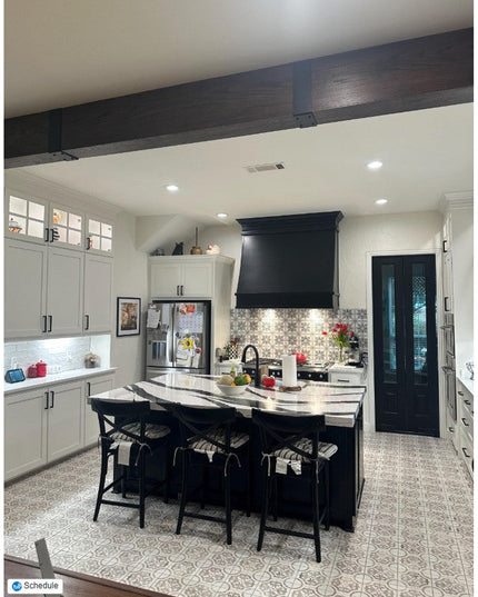 Black decorative wooden beam strap wraps around dark ceiling beam in modern farmhouse kitchen with white cabinets and isla...
