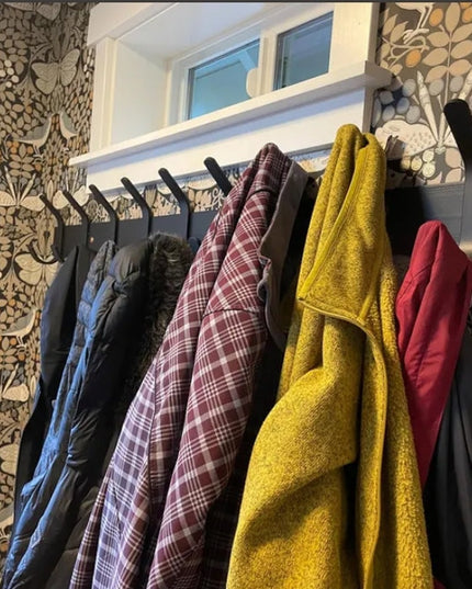 Black metal Fairmount Style Coat Rack by Industrial Farm Co with multiple hooks holding colorful jackets and towels agains...