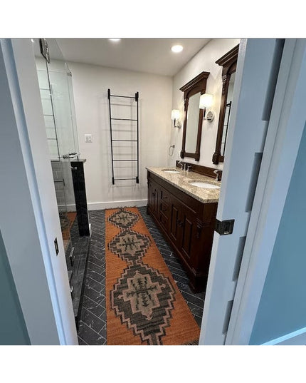 Black metal wall mounted Ossit ladder by Industrial Farm Co displayed in modern bathroom with dark tile flooring and woode...