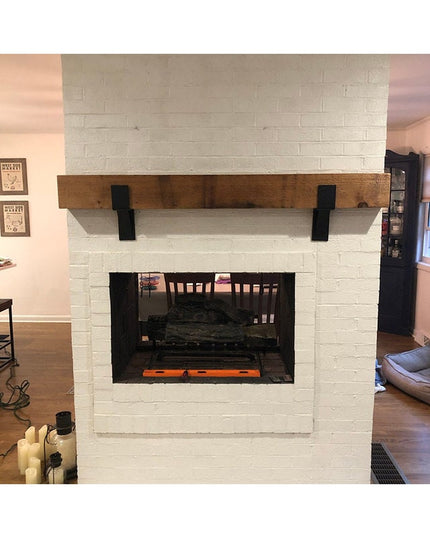 Black metal Seneca 3" farmhouse mantel brackets supporting rustic wood beam on white painted brick fireplace by Industrial...