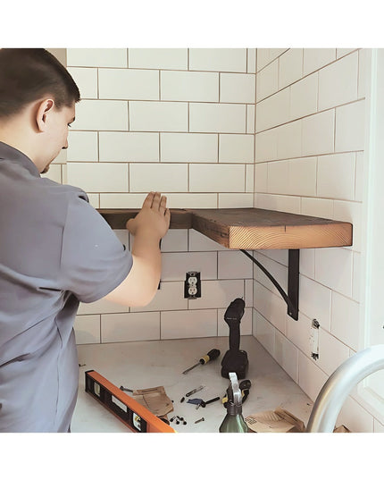Man installing black steel Pops 2 inch industrial shelf bracket with curved support bar under wooden floating shelf in whi...