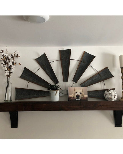 Black metal floating mantel shelf brackets supporting dark wood beam with decorative windmill wall art, vase, and cotton s...