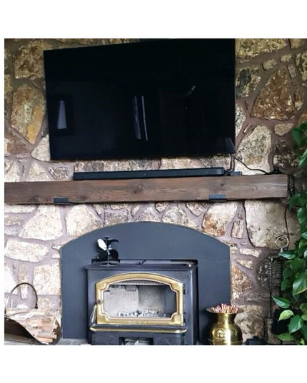 Rustic wood mantel shelf with dark metal brackets mounted on natural stone fireplace wall above wood burning stove insert