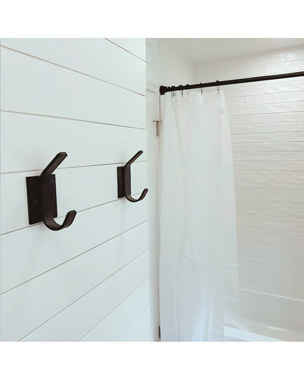 Black metal Elizabeth Wall Hook by Industrial Farm Co mounted on white shiplap bathroom wall next to shower with white cur...