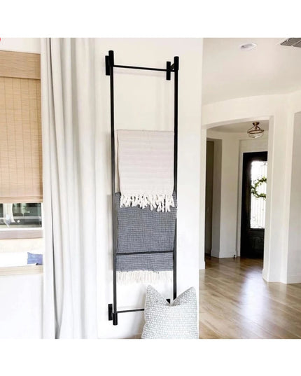 Black metal wall-mounted Ossit ladder by Industrial Farm Co displaying striped throw blankets in modern white living room ...
