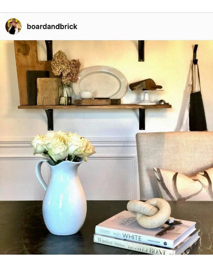 Black curved steel industrial shelf brackets supporting wooden shelf with white dishes and decor in farmhouse kitchen setting